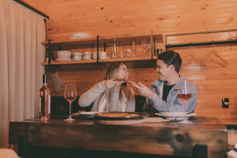 A couple enjoying pizza and wine at a rustic wooden table in a cozy setting.